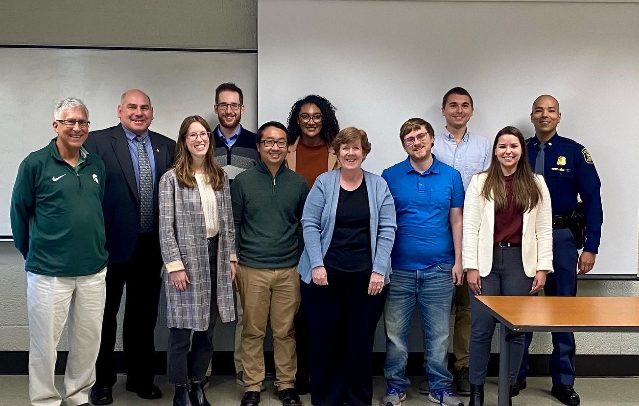 Org Psych students and Michigan State Police representatives smile for the camera in a classroom