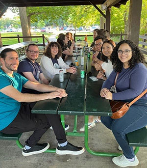 Clinical Science faculty and students sit at a picnic table and look at the camera.