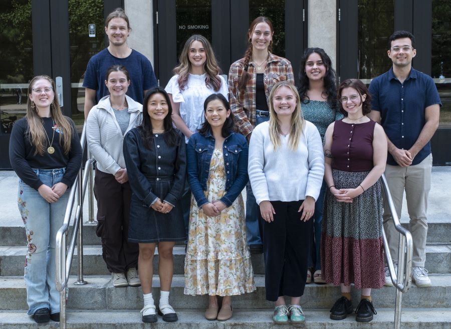 A group of graduate students smile for the camera while on the front steps of the Psychology building.