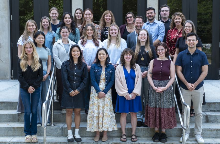 A group of faculty and graduate students smile for the camera while on the front steps of the Psychology building.
