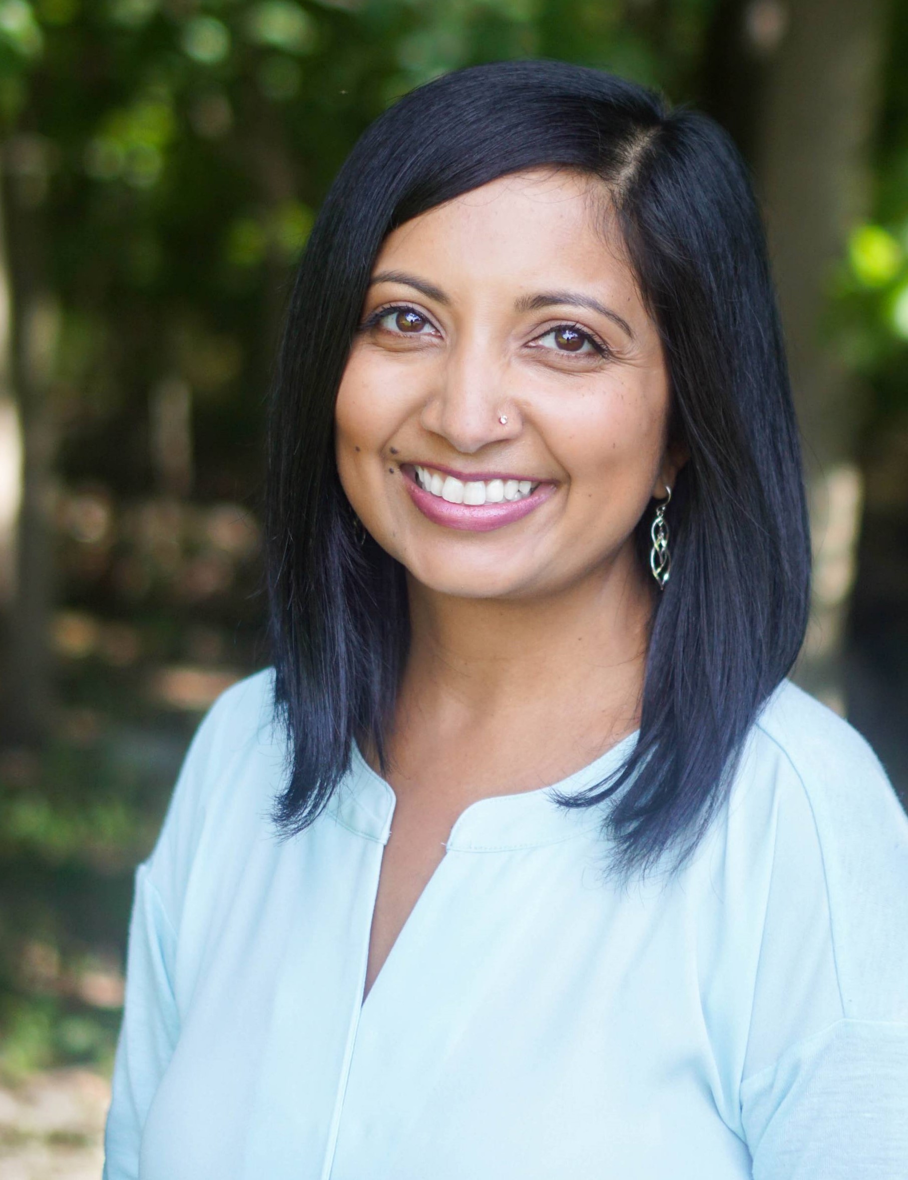 Wearing a light blue shirt, Mikhila Wildey smiles directly at the camera while outside.