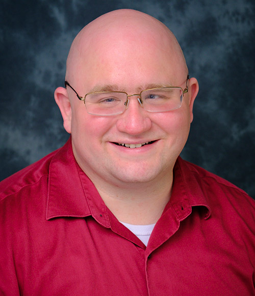 A headshot of Dr. William Chopik. He's smiling directly at the camera. He's wearing a red shirt.