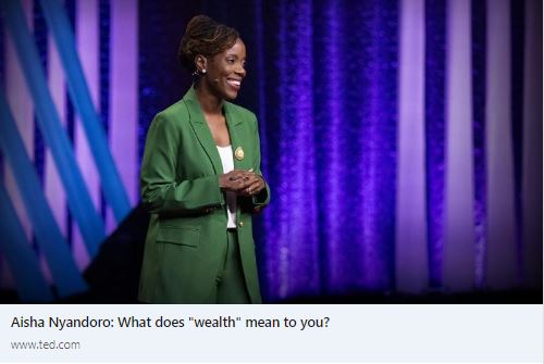 Dr. Aisha Nyandoro wears a green pantsuit and stands on the Ted Talk stage. She smiles at the non-visible audience. 