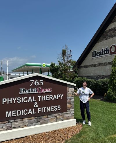 Hanna Kemenah stands in front of a health Quest Physical Therapy sign.