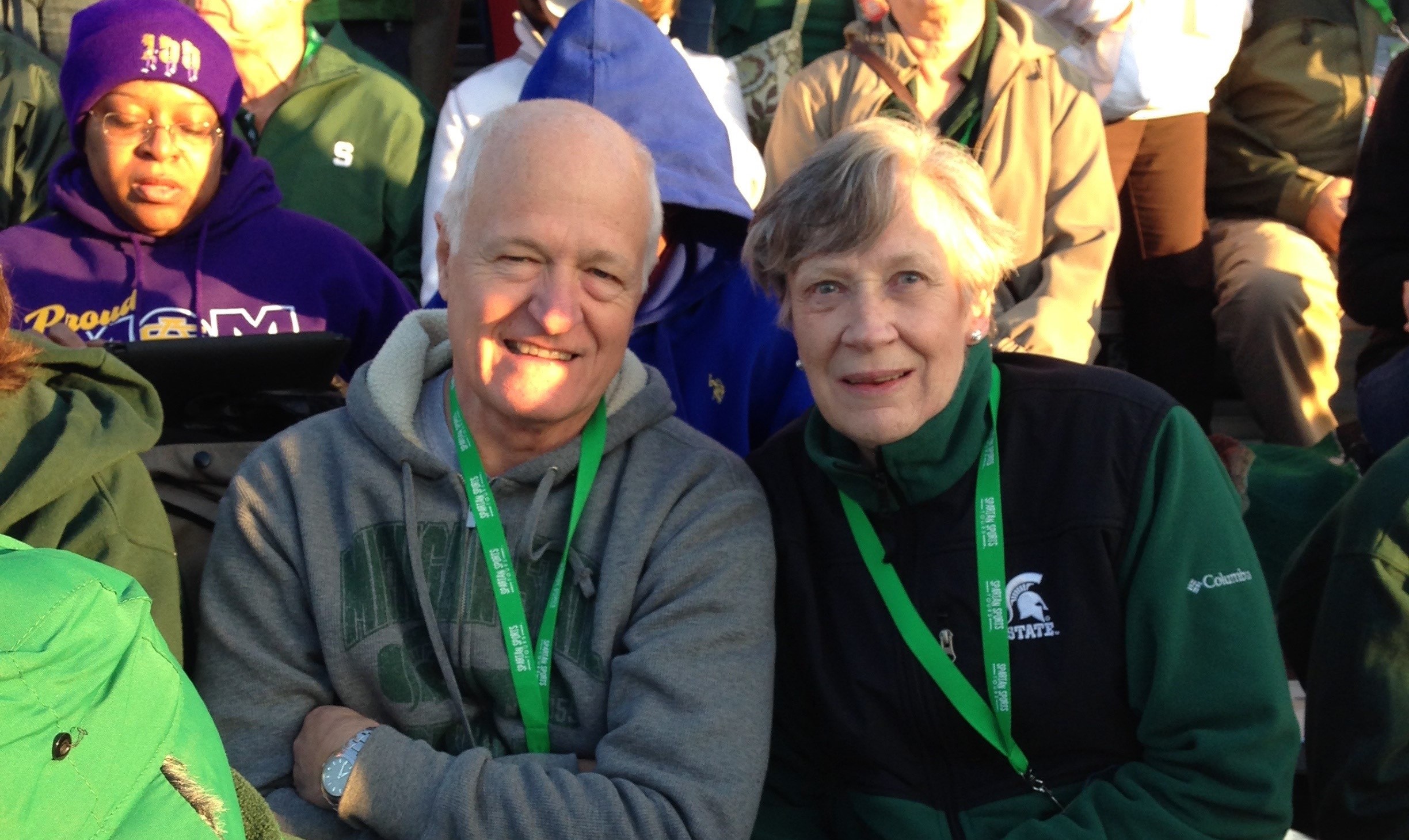 Dr. Neal Schmitt and Dr. Kara Schmitt smile at the camera while in the stands of a sporting event. They wear Spartan gear. 